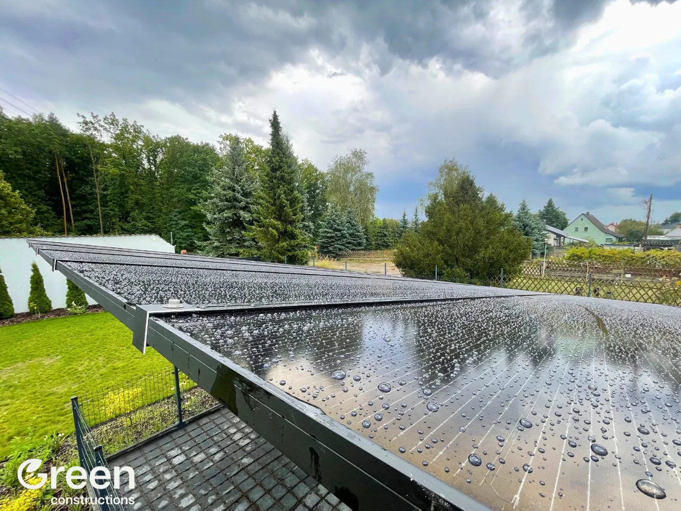 Dach wiaty fotowoltaicznej po burzy - widoczne chmury burzowe oraz krople wody na powierzchni paneli fotowoltaicznych.