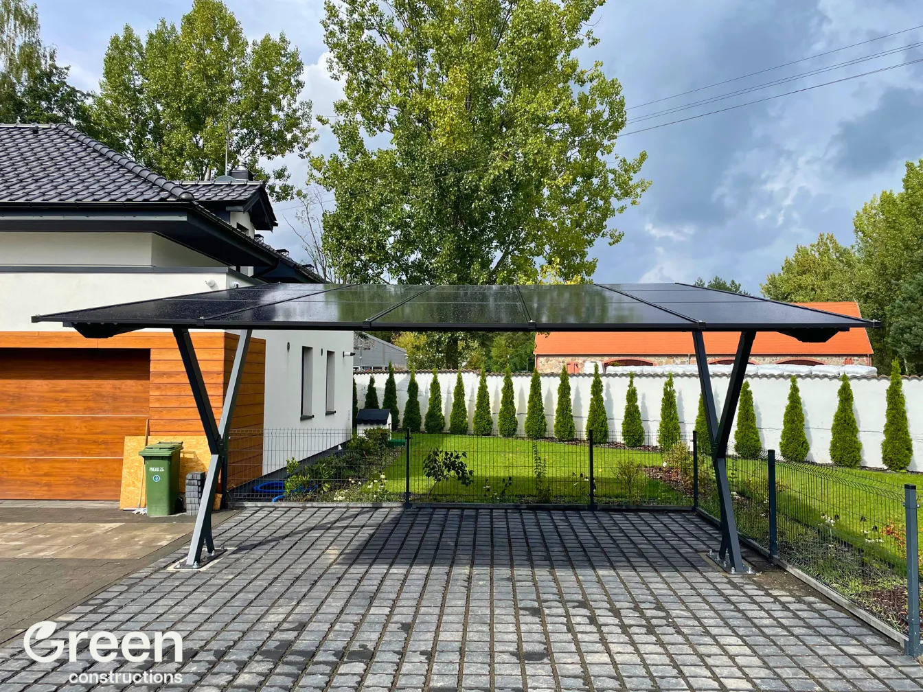 Carport PV o mocy 7,5 kWp na podjeździe z kostki brukowej obok domku jednorodzinnego. Konstrukcja stalowa pomalowana na kolor antracyt.