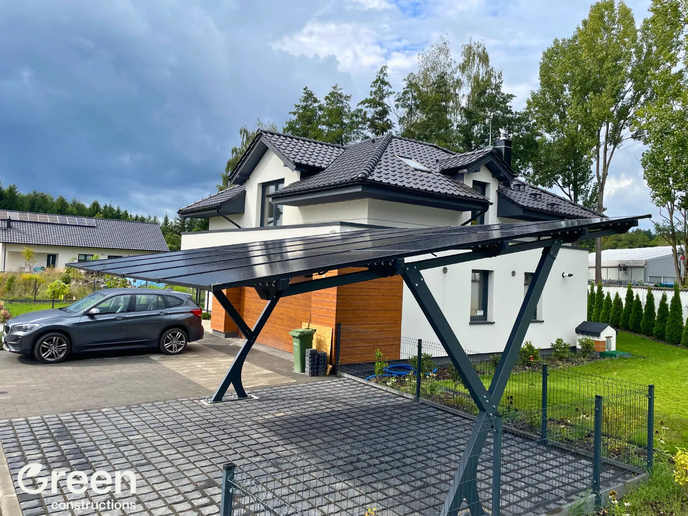 Widok po przekątnej na Wiatę fotowoltaiczna o mocy 7,5 kWp obok domku jednorodzinnego, na podjeździe stoi samochód marki BMW.